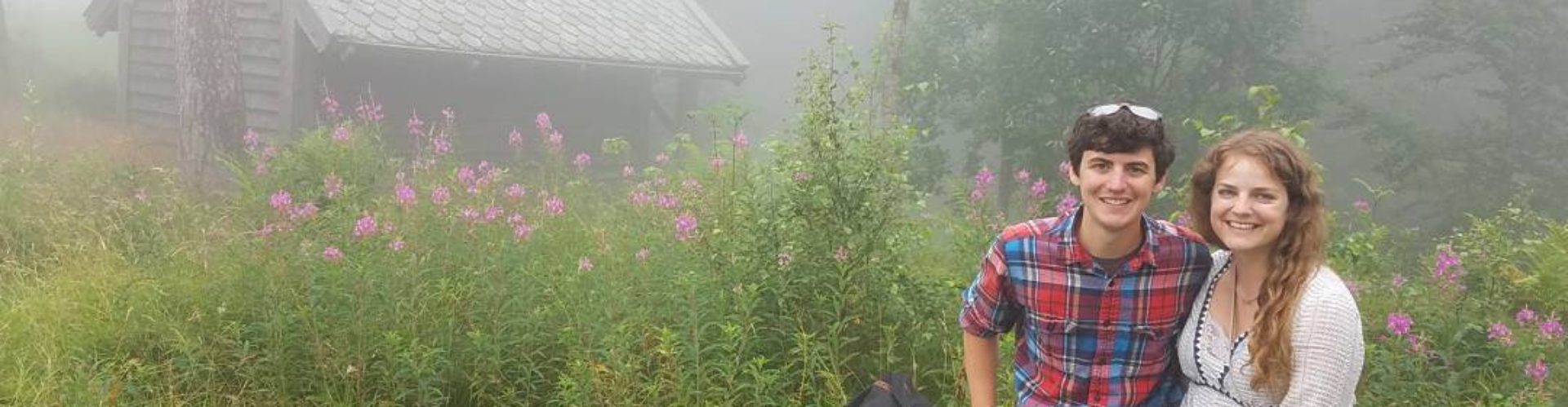 Chris standing in a field with wildflowers and a cabin in the background.